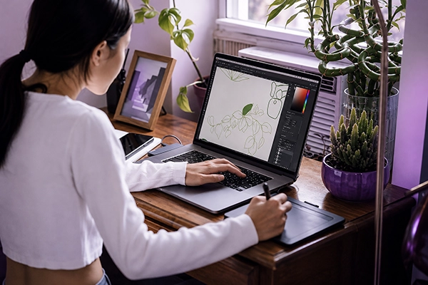 Vrouw werkt met een laptop en tekentablet aan een digitale plantenillustratie in een creatieve werkplek